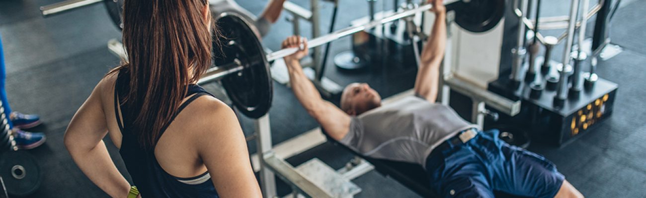 Woman trainer spotting man doing bench press