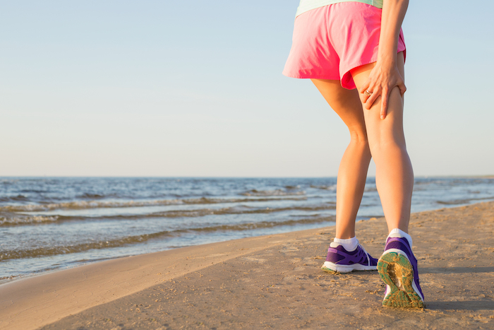 woman grabbing back of leg beach | sore hamstrings