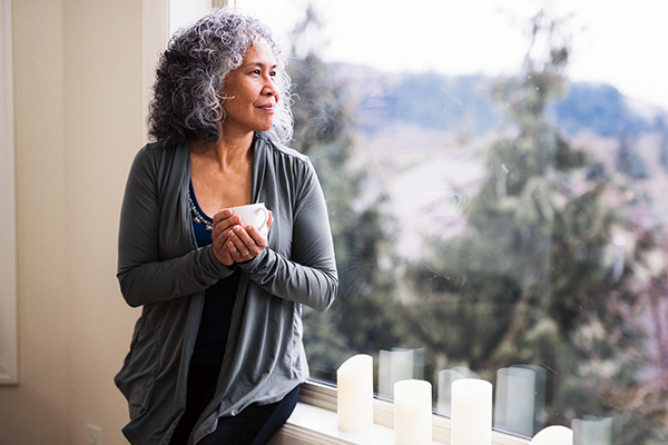 Older woman holding coffee, looking out window