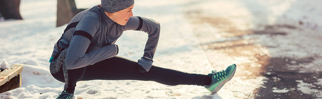 woman stretching outside before snowy run | holiday fitness