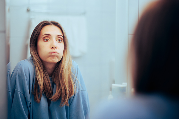 woman staring at mirror puffing in distress | toxic positivity