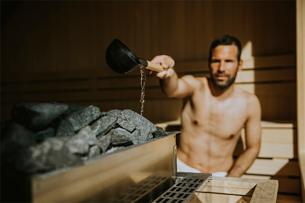 man putting water on rocks in sauna | Sauna Before or After Workout