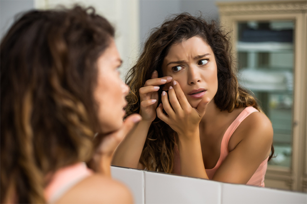 woman popping pimple in mirror | Body Dysmorphia