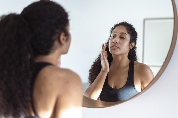 woman checking skin in mirror | Effects of Sugar on Skin