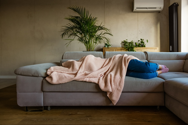 Woman sleeps on the sofa holding blanket over head | hangover recovery