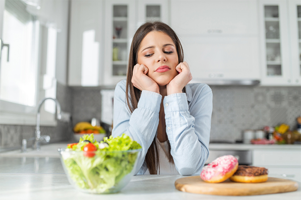 sad woman looking at salad and donuts | Orthorexia