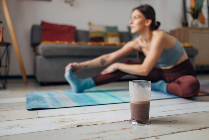 woman stretching at home with protein shake | When Is the Best Time to Drink a Protein Shake