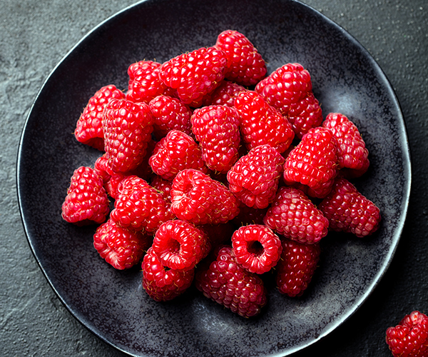 Fresh raspberries in a black bowl.