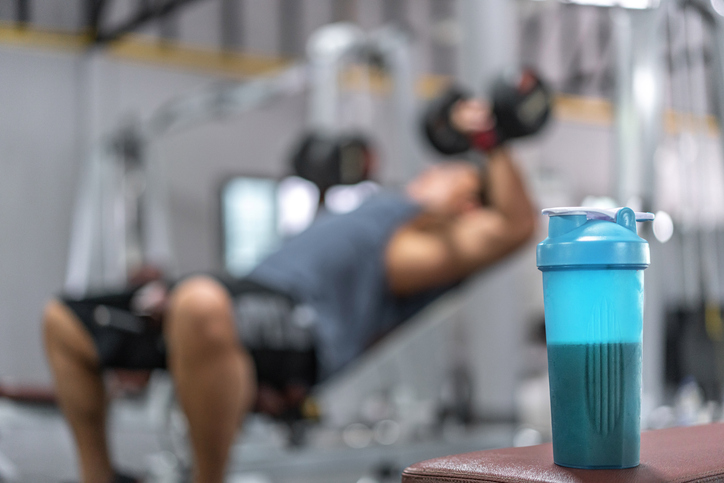 man lifting weights with protein bottle in foreground | Anabolic window